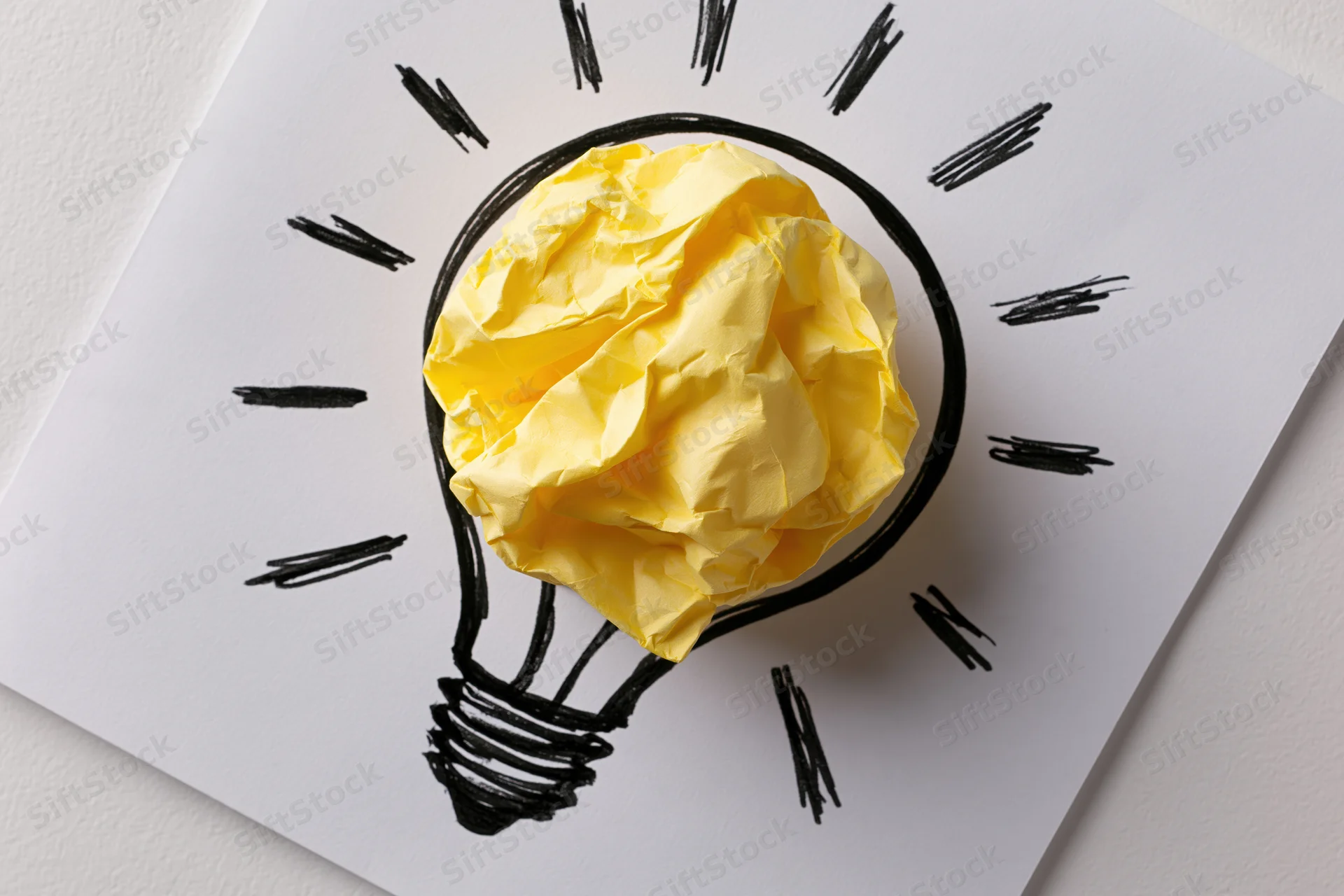 Crumpled yellow paper ball inside hand-drawn lightbulb on white paper