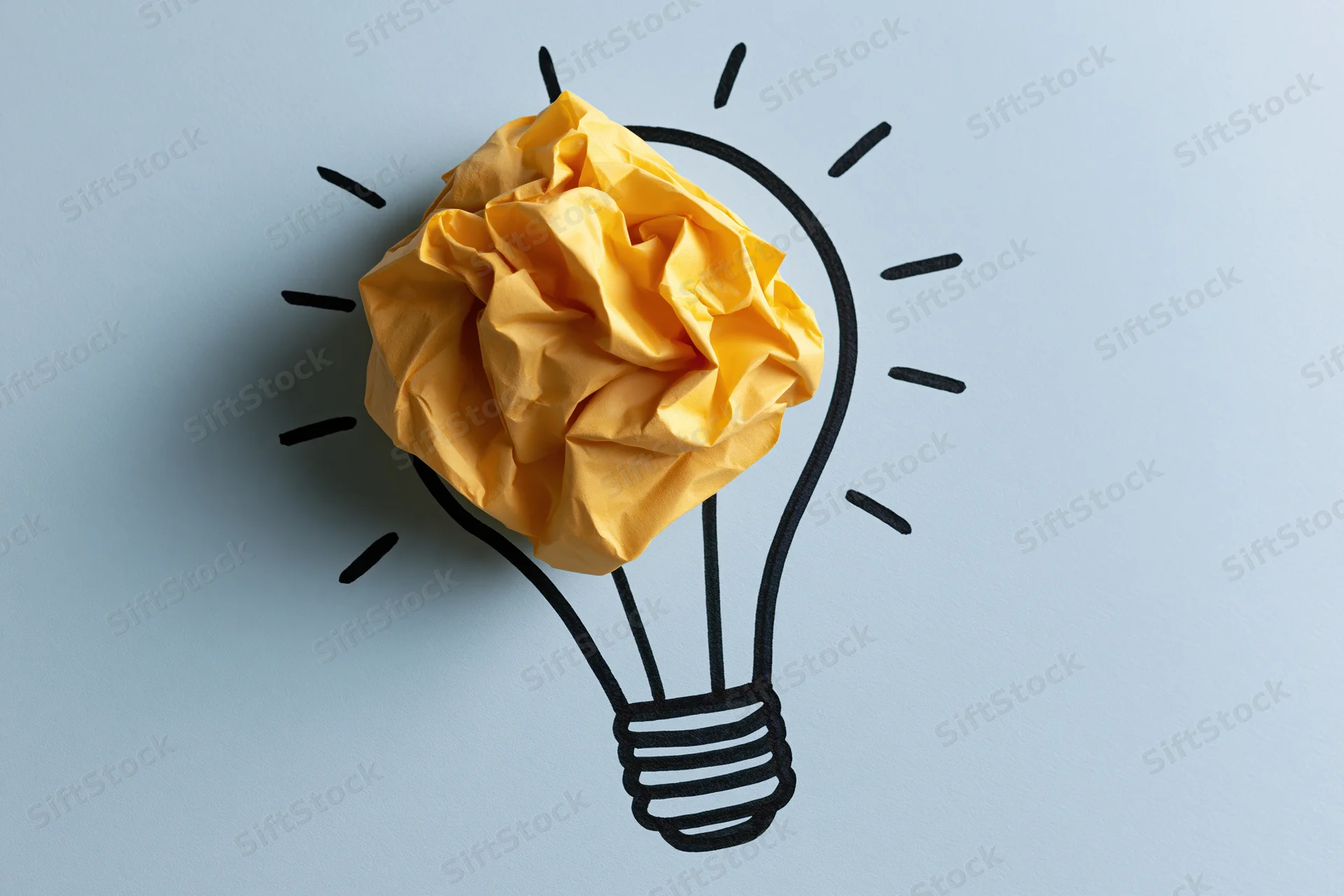 Crumpled yellow paper ball placed inside hand-drawn lightbulb outline on light blue background