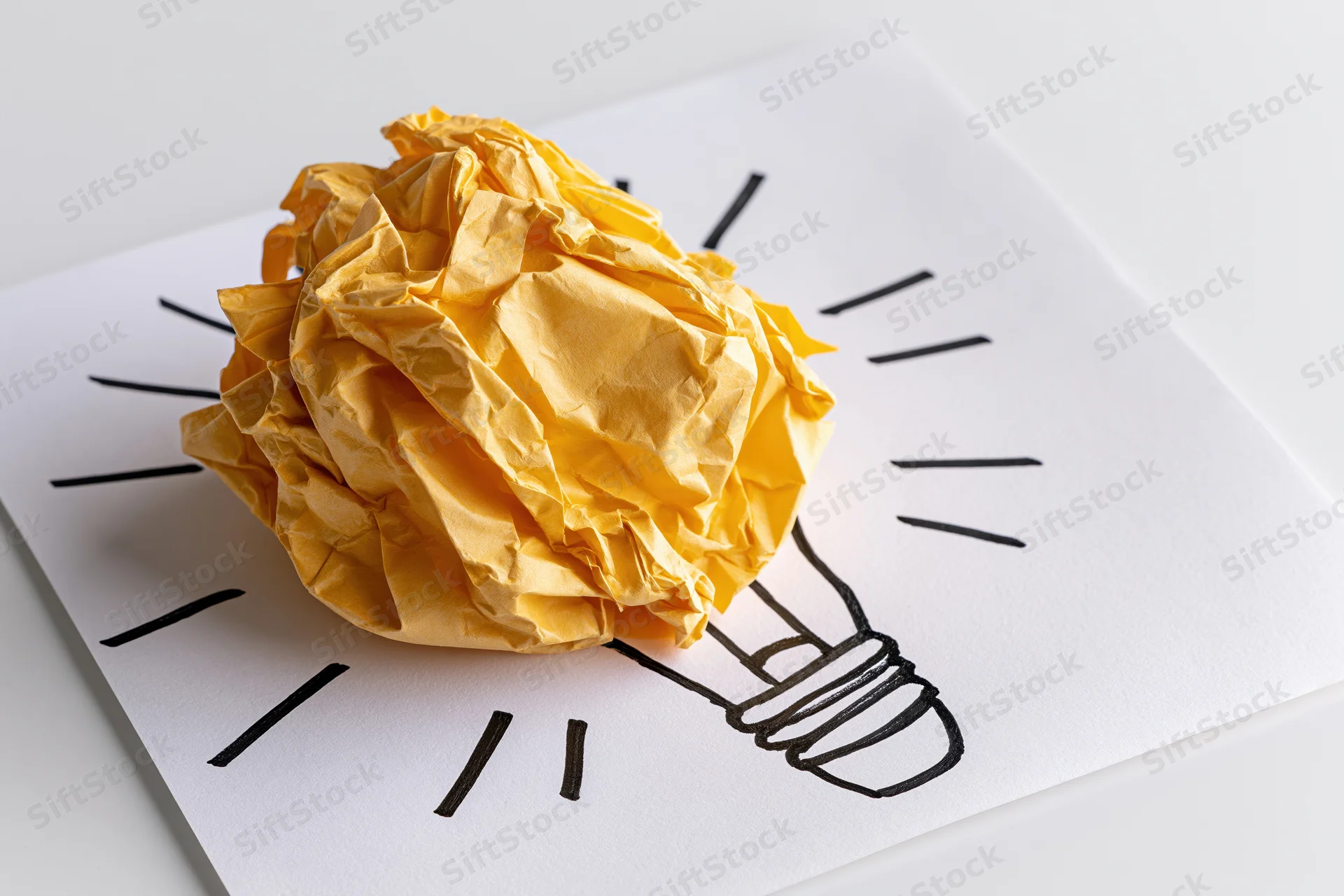Crumpled yellow paper ball placed on a hand-drawn lightbulb sketch on white paper
