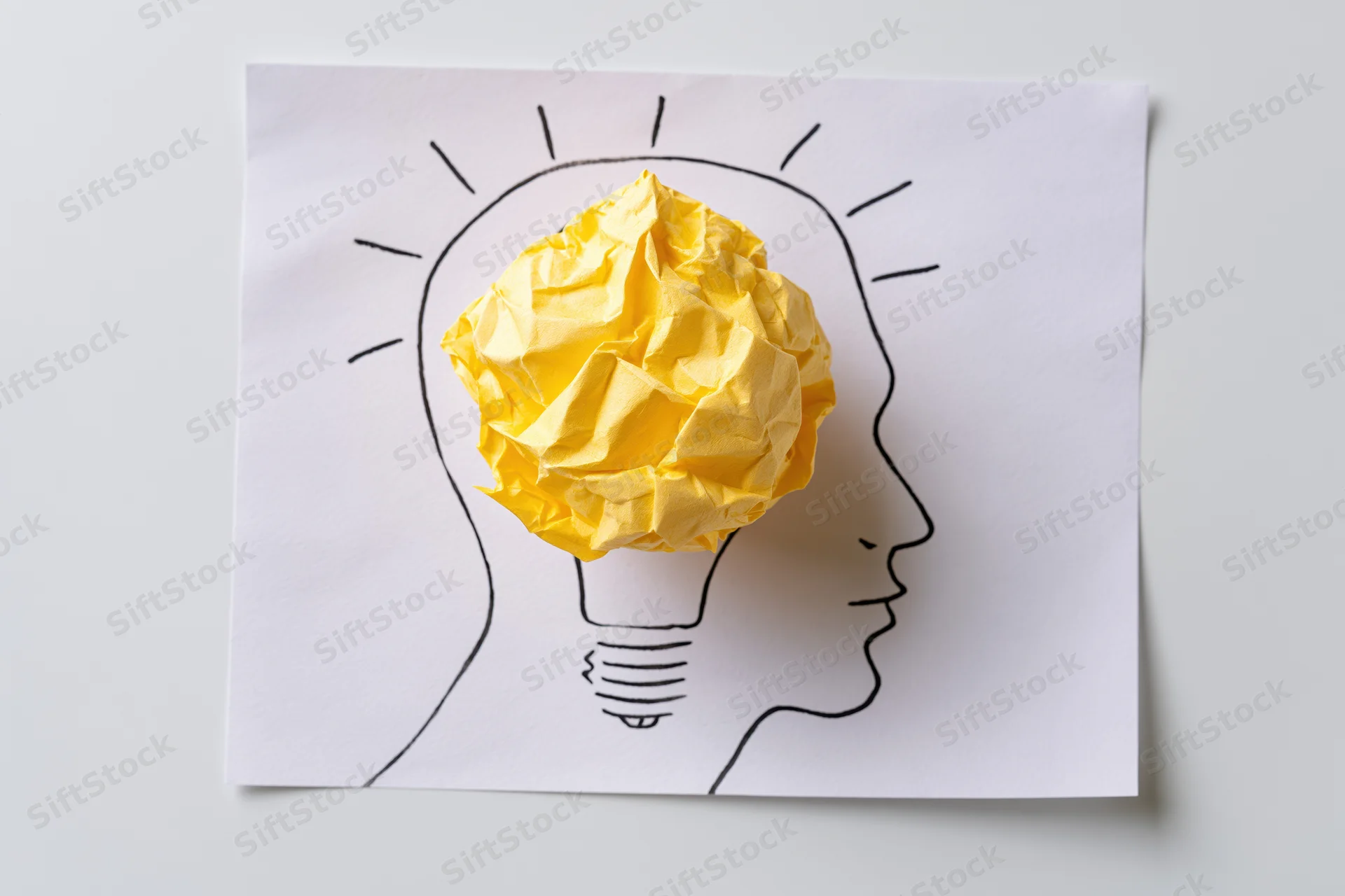 Crumpled yellow paper ball as lightbulb inside drawn head profile on white paper