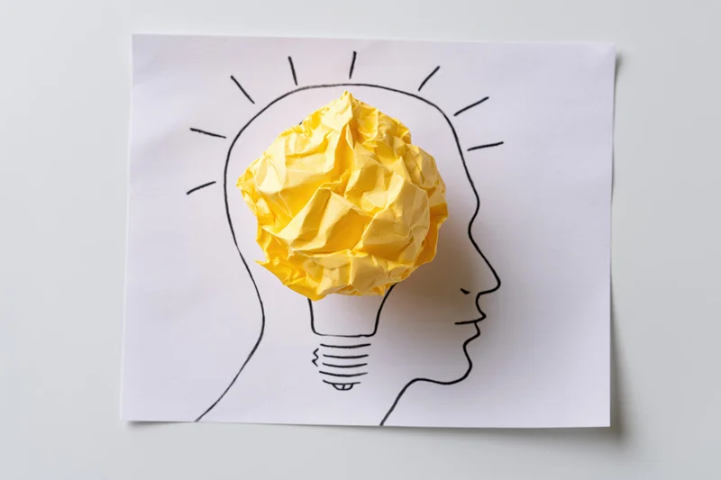 Crumpled yellow paper ball as lightbulb inside drawn head profile on white paper