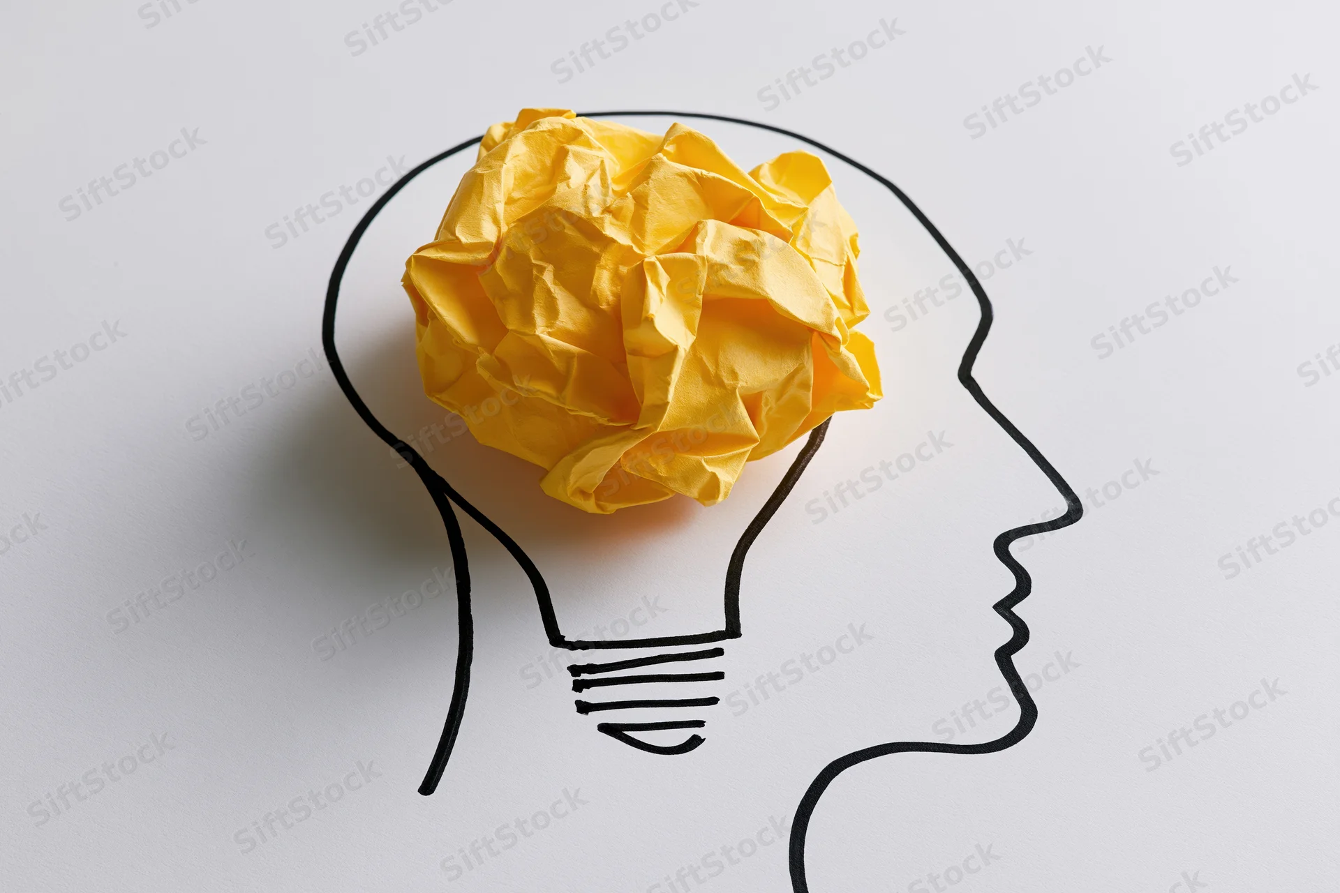 Crumpled yellow paper ball inside a drawn lightbulb-shaped head outline on white background