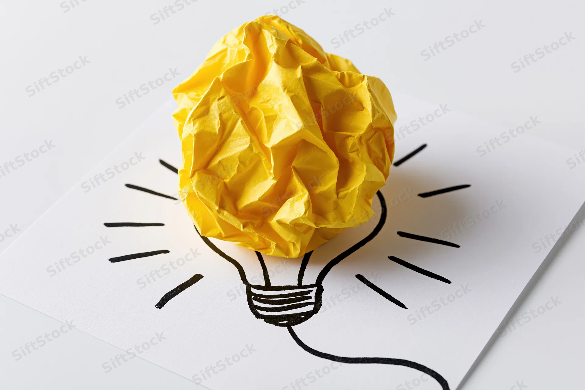 Crumpled yellow paper ball placed on a hand-drawn lightbulb sketch on white paper