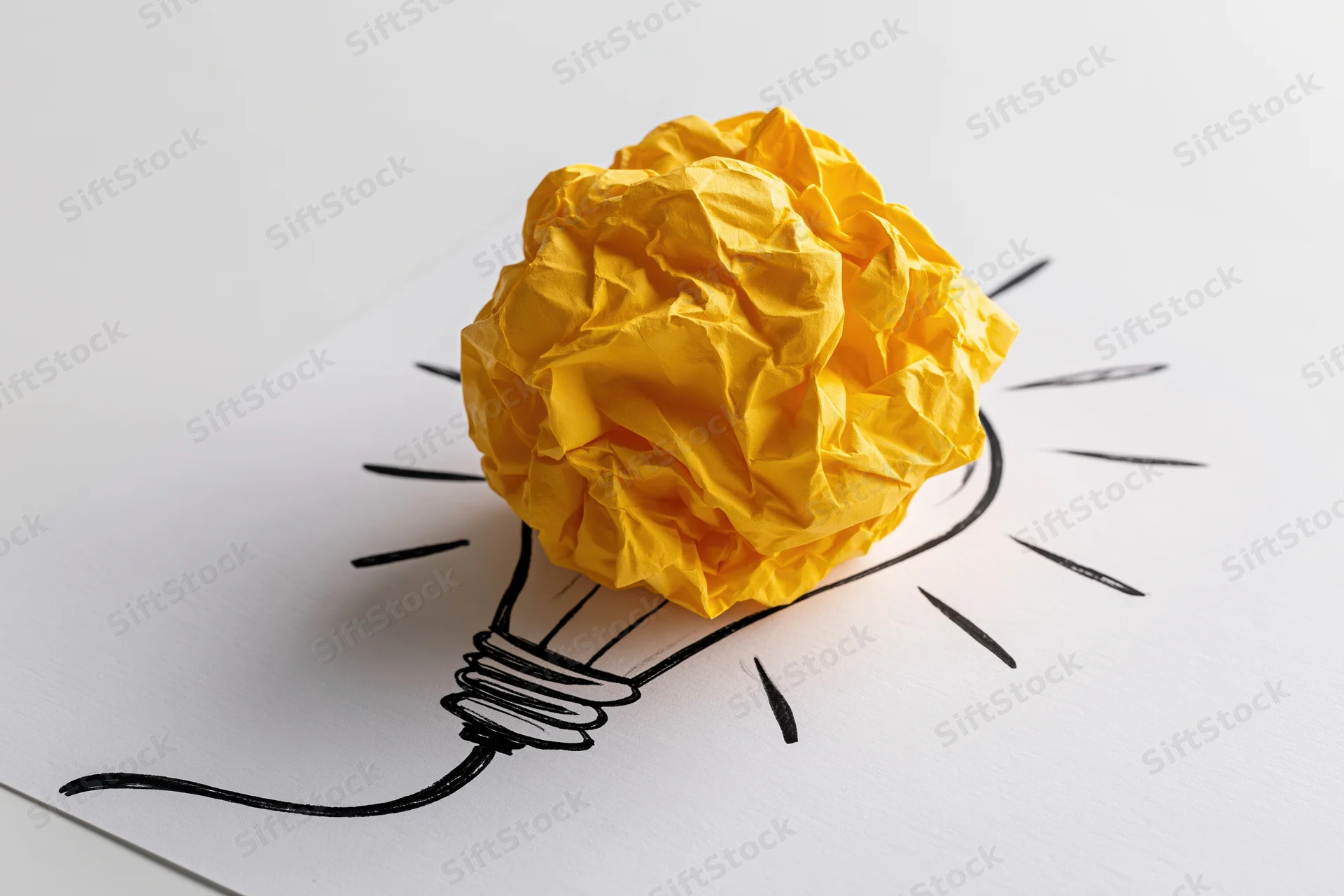 Crumpled yellow paper ball placed on hand-drawn lightbulb sketch on white paper