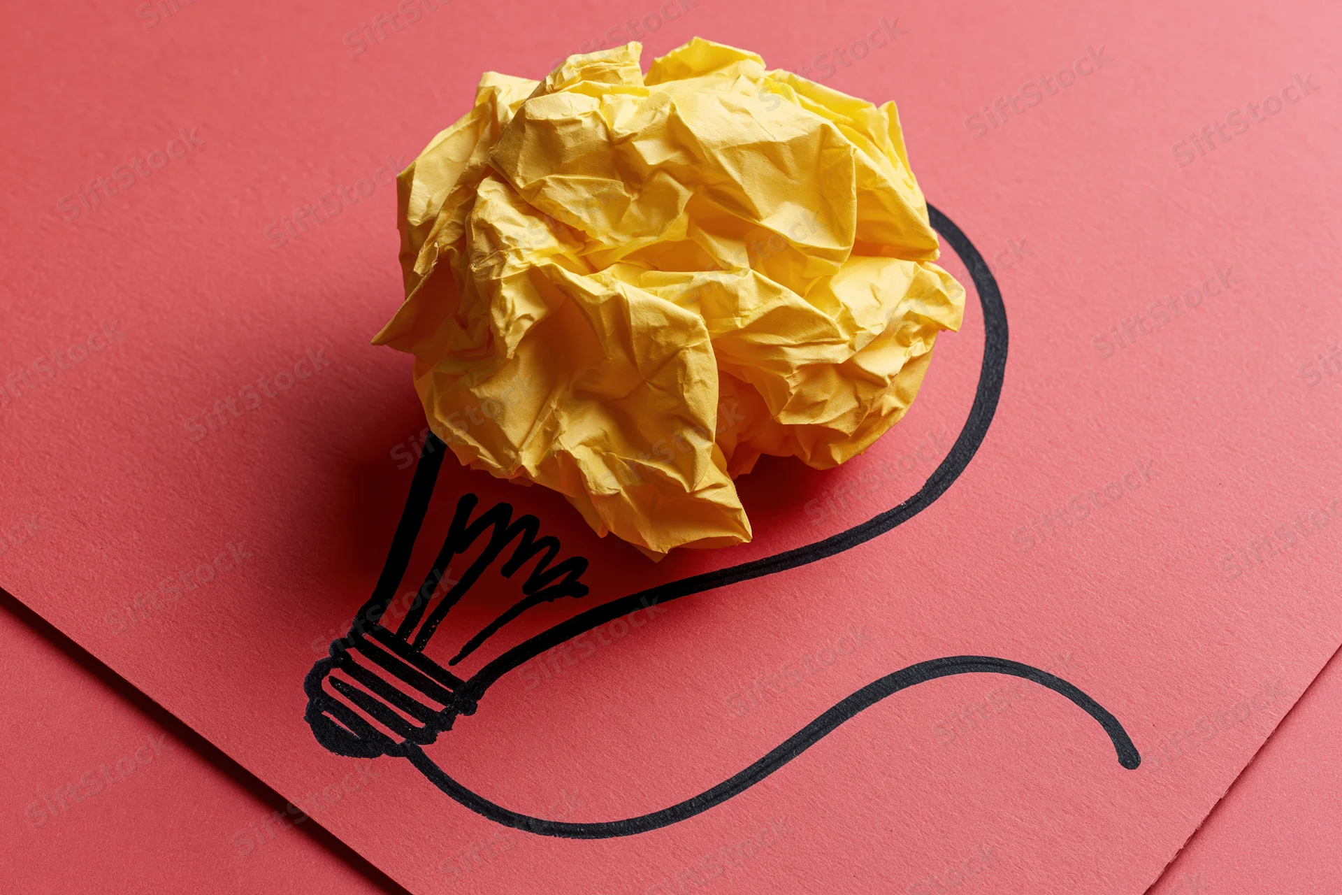 Crumpled yellow paper ball placed on red cardboard with hand-drawn lightbulb outline