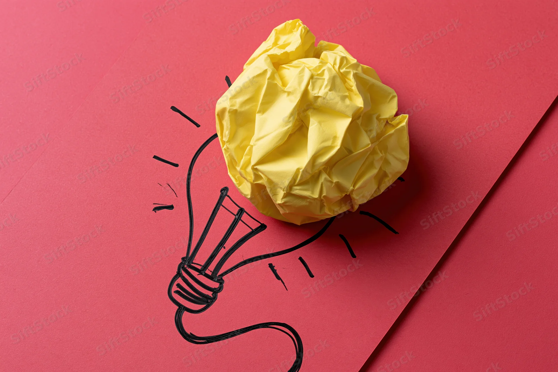 Crumpled yellow paper ball on red cardboard with hand-drawn lightbulb sketch