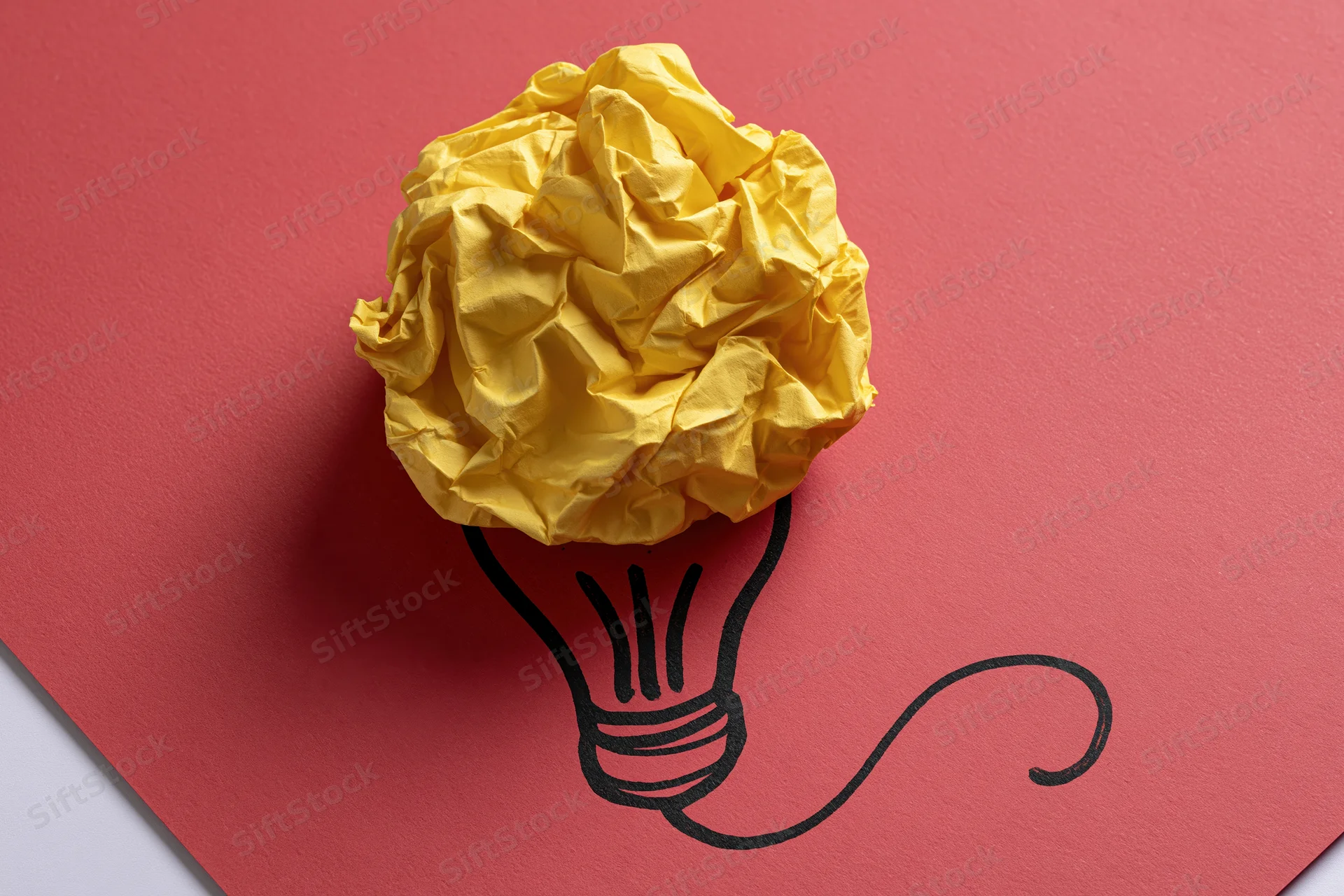 Crumpled yellow paper ball placed on red cardboard with hand-drawn lightbulb outline