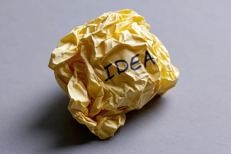Crumpled yellow paper ball with handwritten idea on gray surface