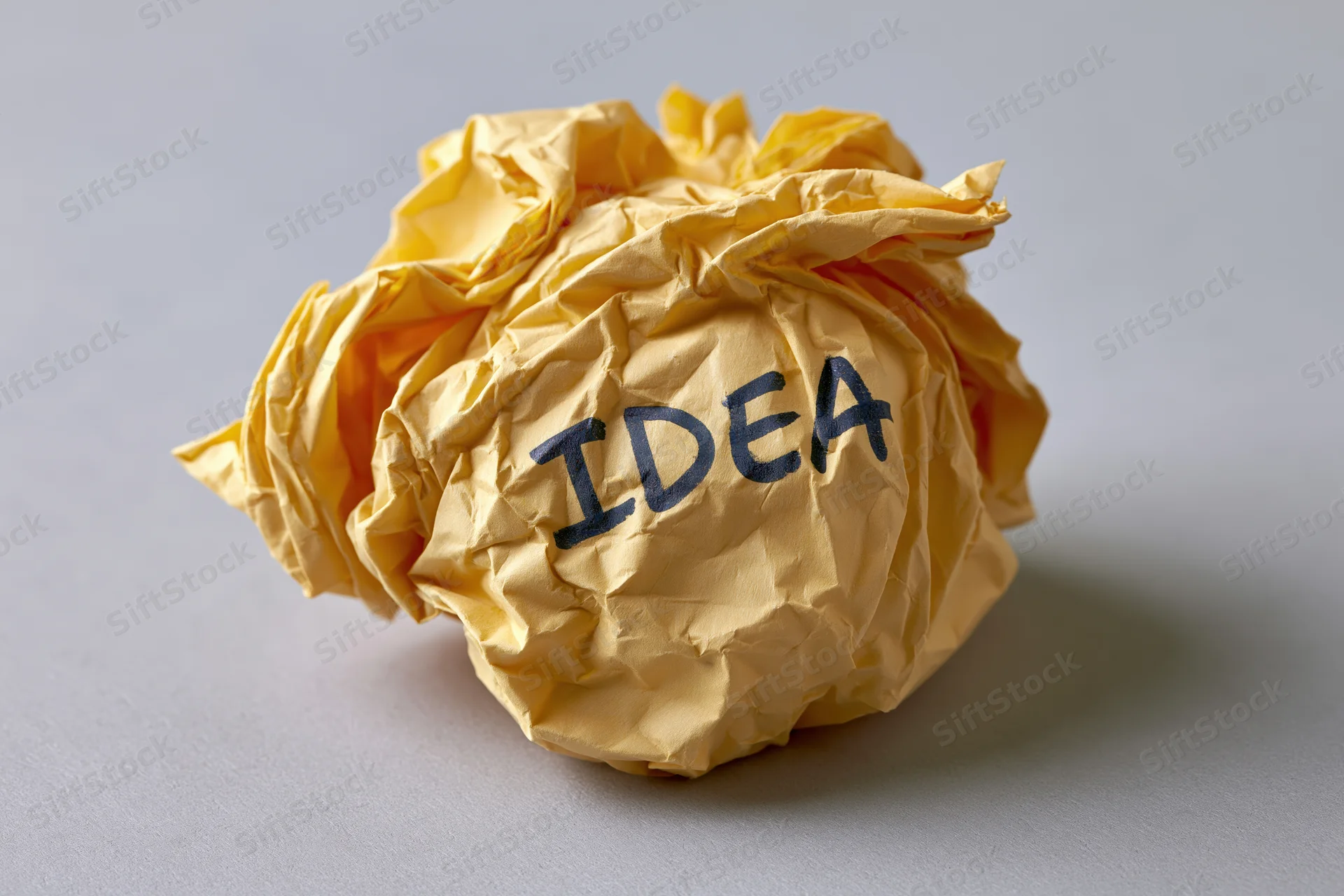 Crumpled yellow paper ball with handwritten idea text on gray surface