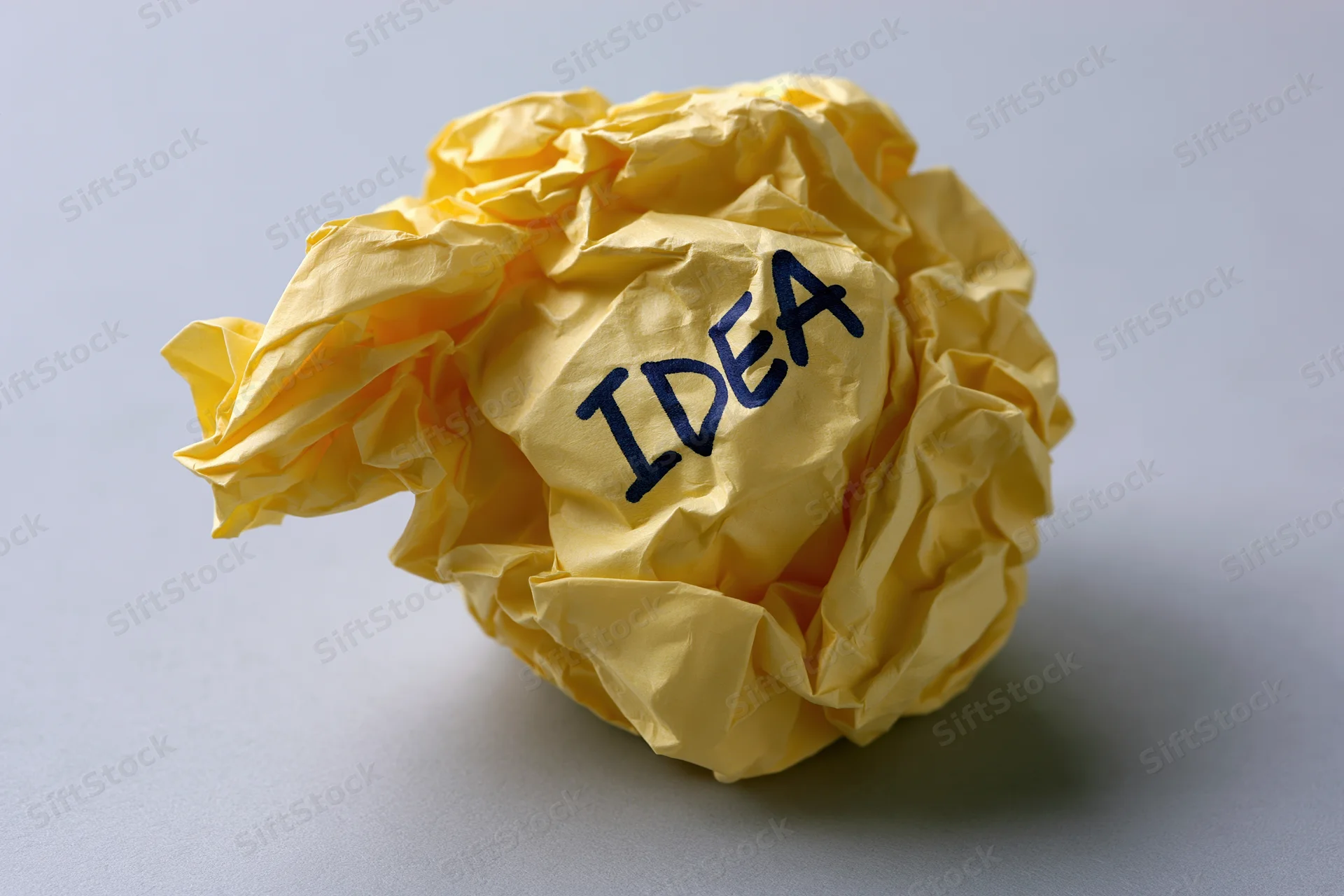 Crumpled yellow paper ball with handwritten idea text on gray surface