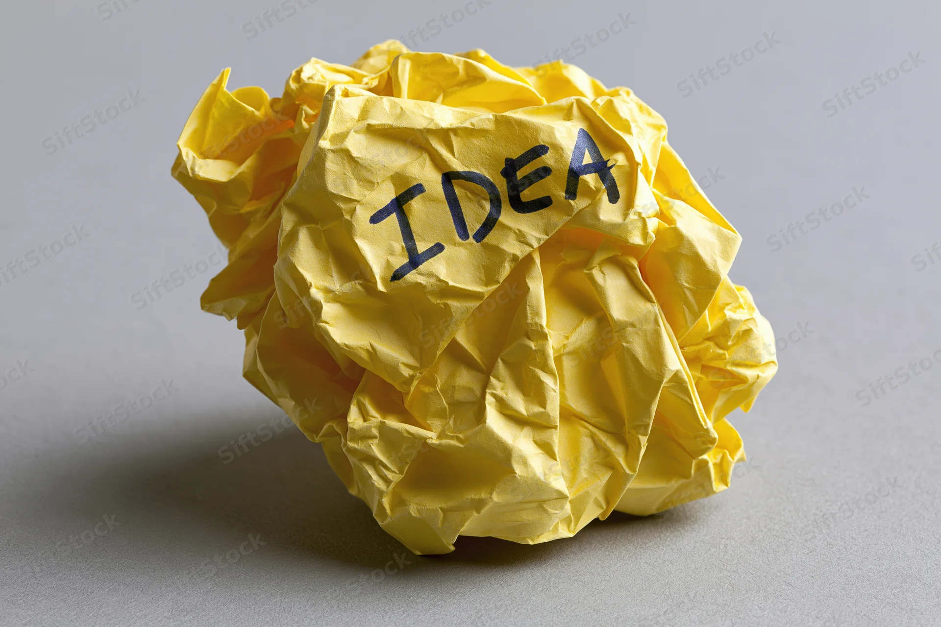 Crumpled yellow paper ball with handwritten idea on gray surface