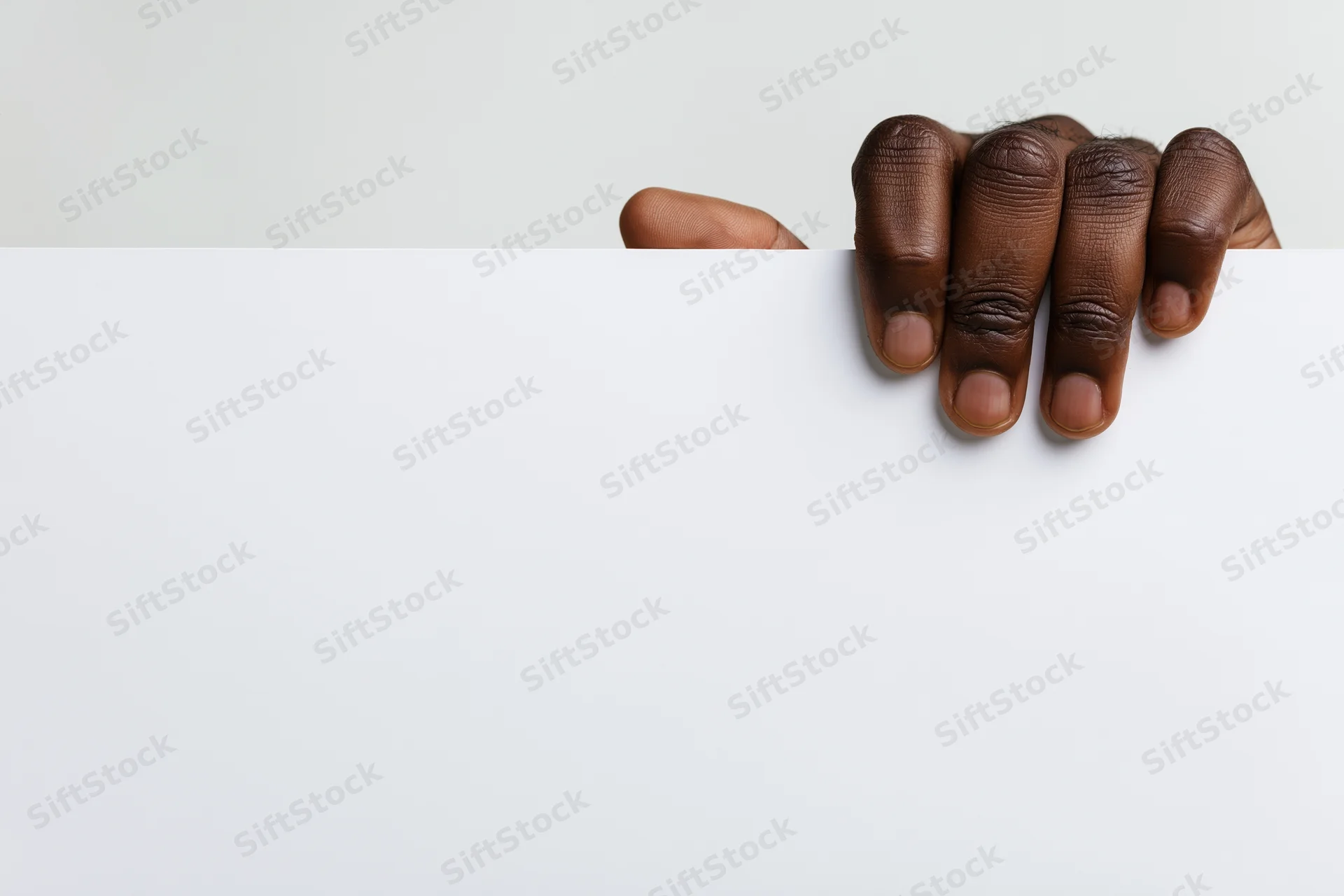 Dark-skinned hand gripping top edge of blank white paper with copyspace below