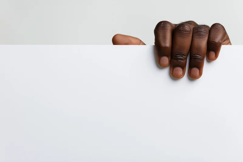 Dark-skinned hand gripping top edge of blank white paper with copyspace below