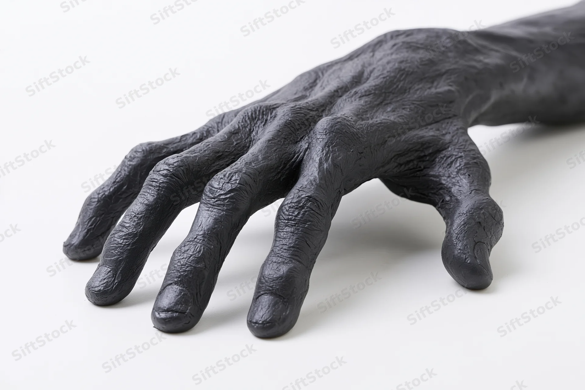Black matte sculptural hand prop crawling on fingers against white background
