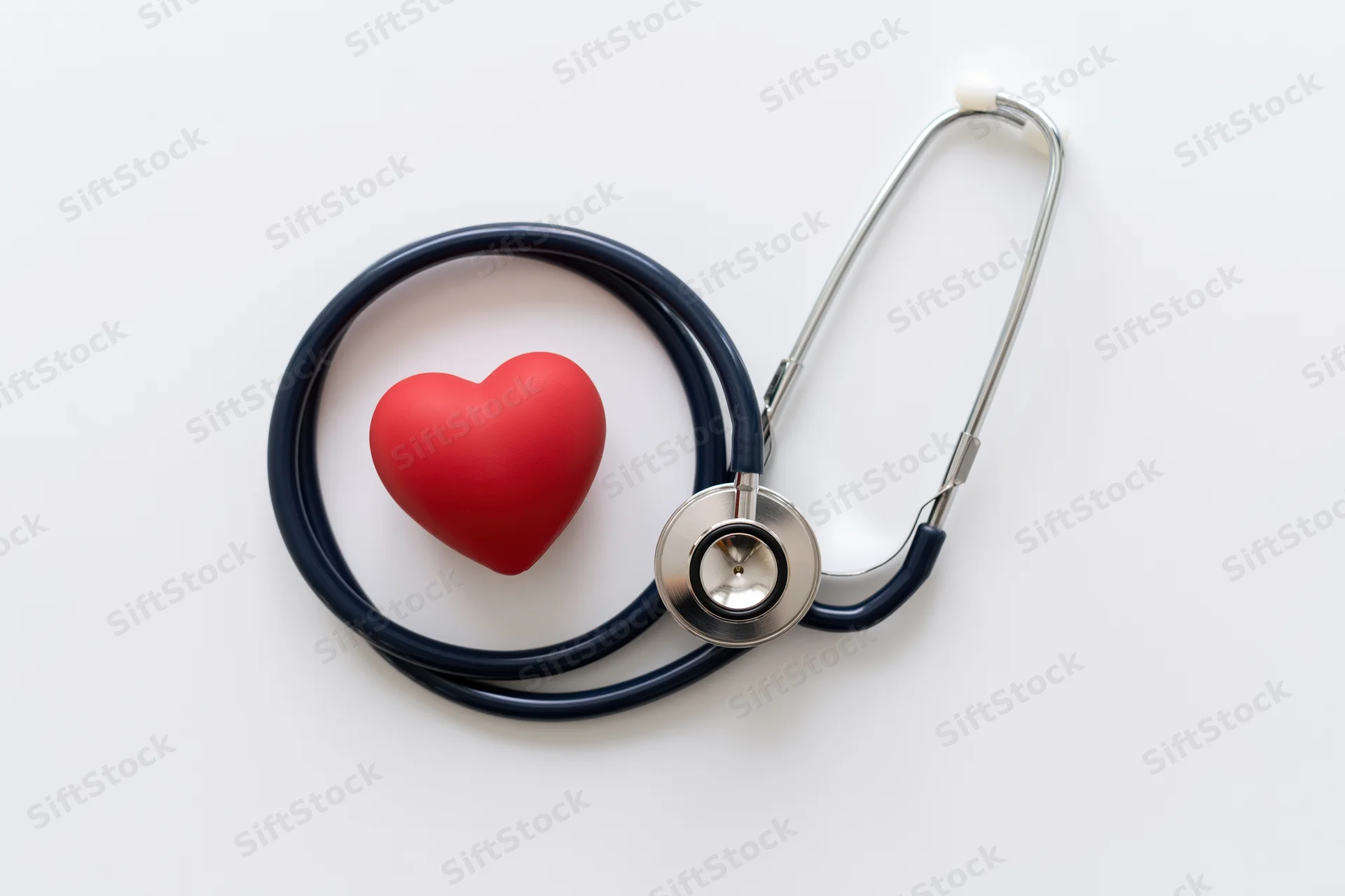 Coiled navy stethoscope beside red rubber heart on white surface