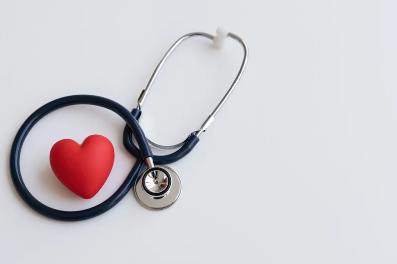 Dark navy stethoscope coiled beside a small red rubber heart on white surface