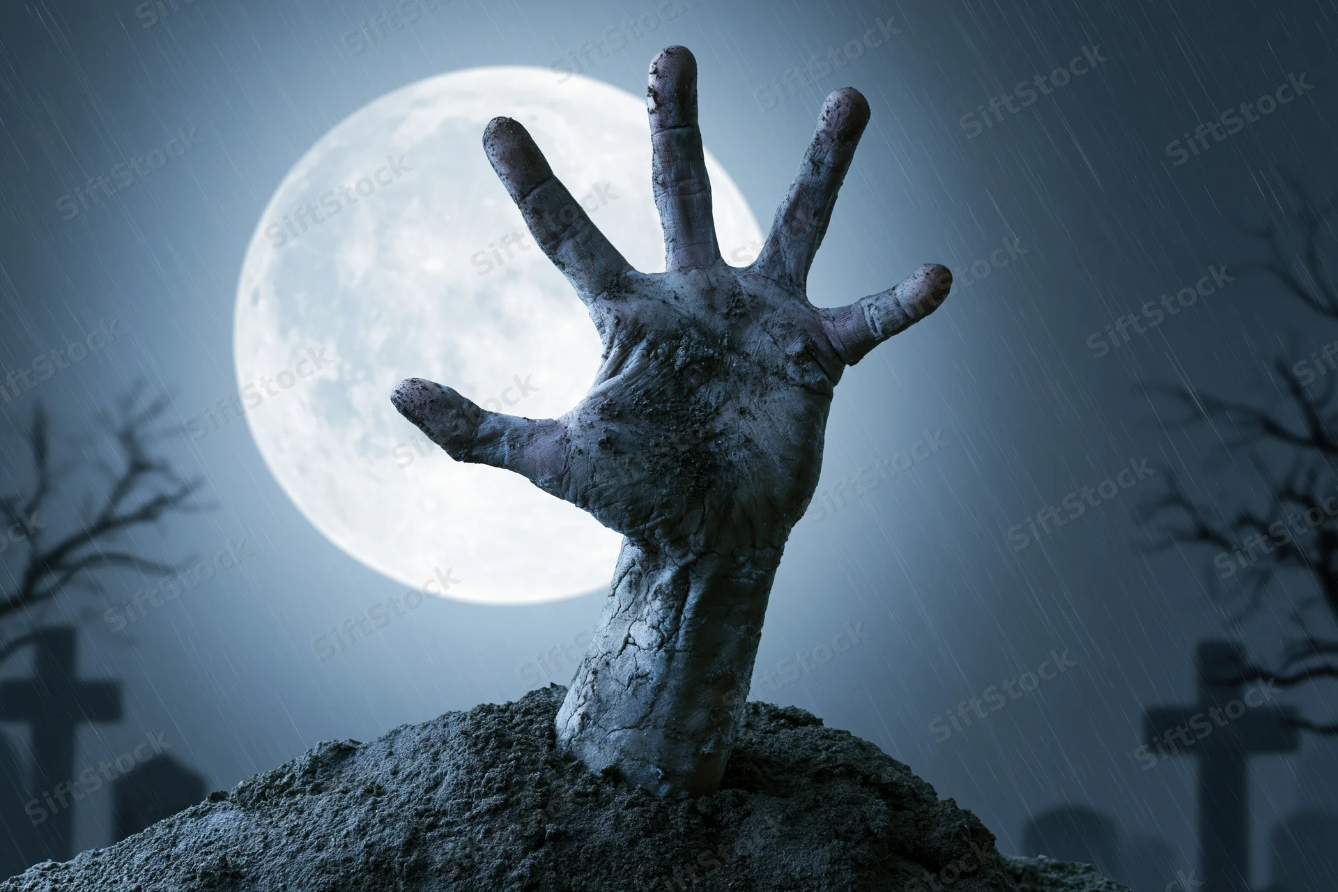Decayed hand emerging from grave soil under full moon in graveyard