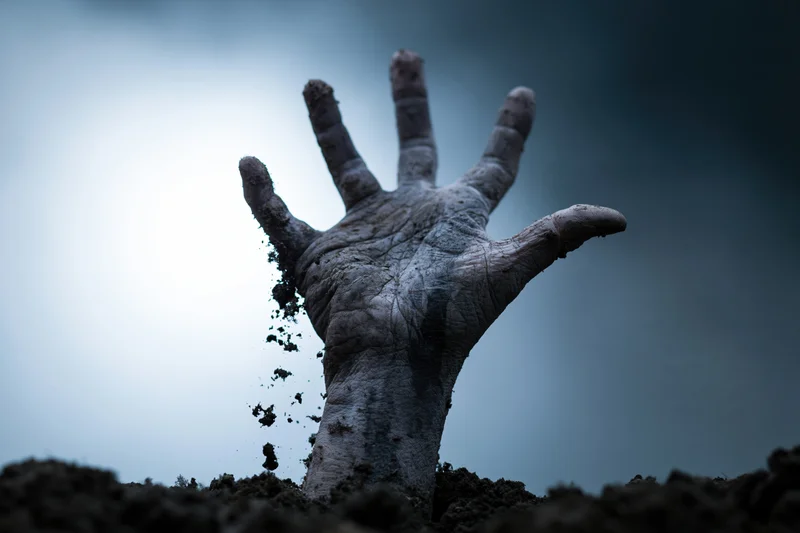 Decayed hand emerging from dark soil with dirt falling from fingers