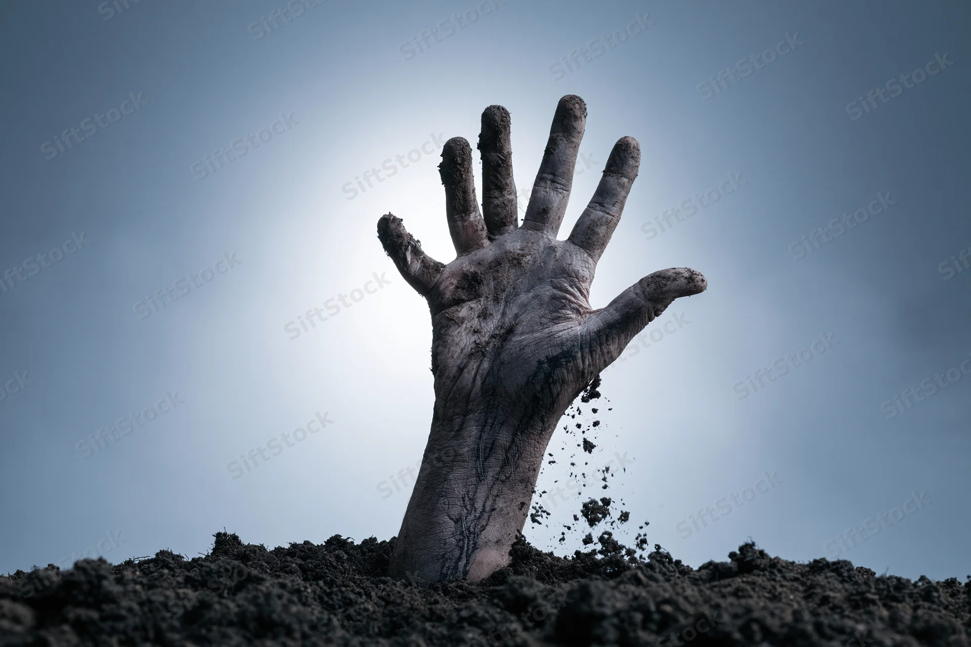 Decayed hand emerging from dark soil against overcast sky