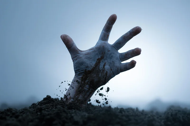 Decayed hand emerging from dark soil in foggy outdoor setting