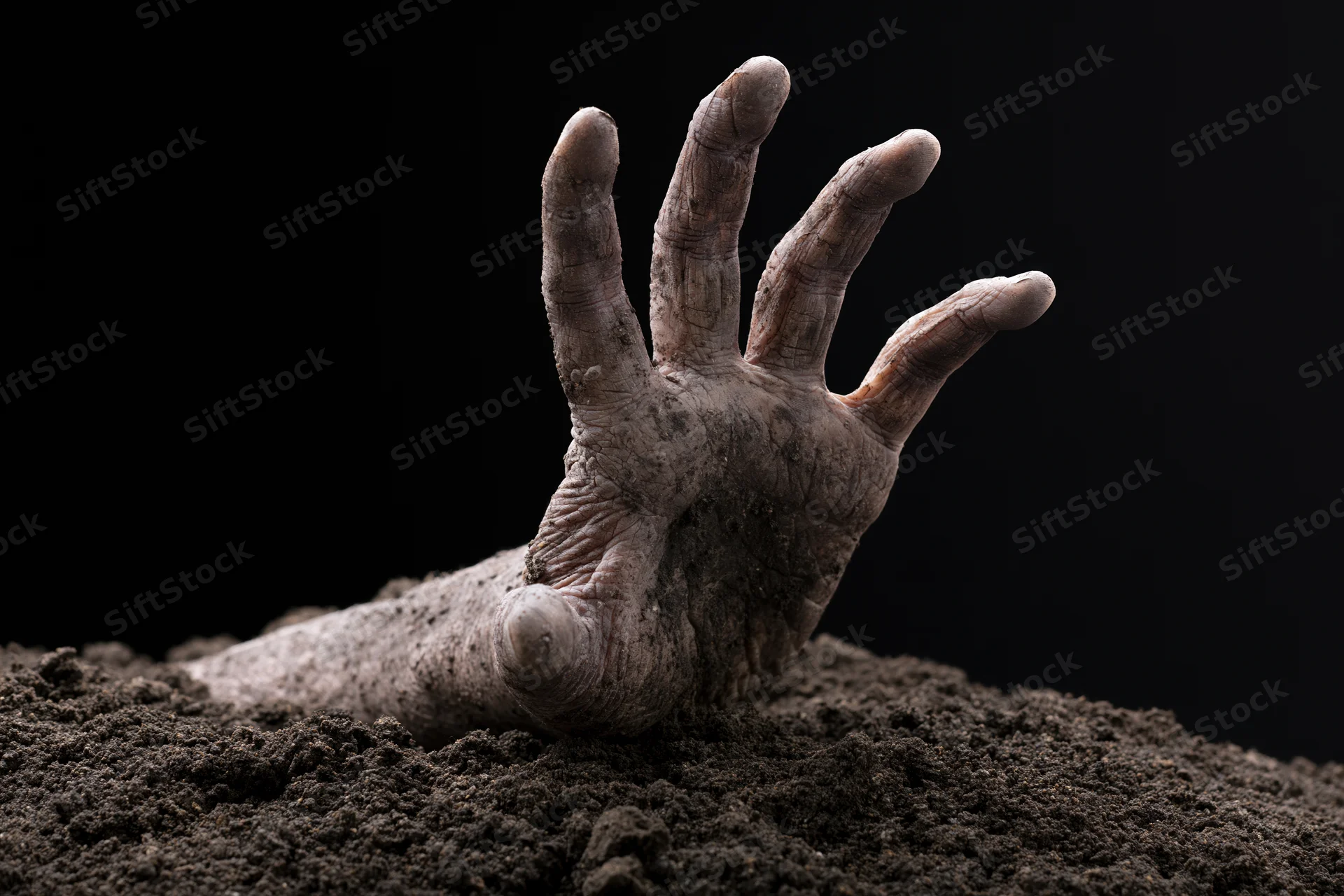 Decayed dirt-covered hand clawing upward from a mound of soil against black background