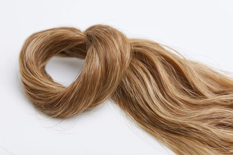 A loose wavy lock of light brown human hair styled into a coil on a white surface