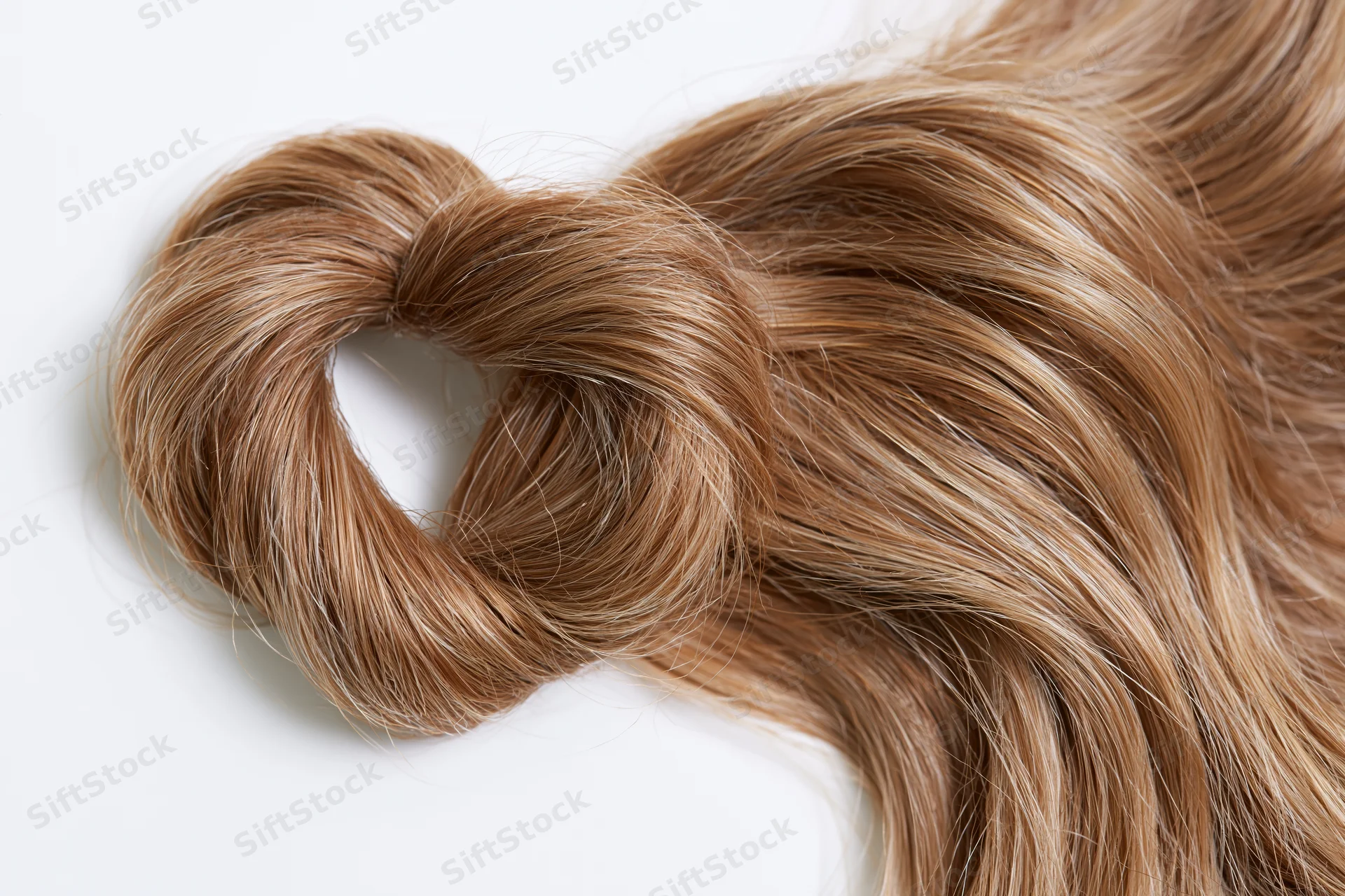 A loose wavy lock of light brown human hair styled into a curl on a white background