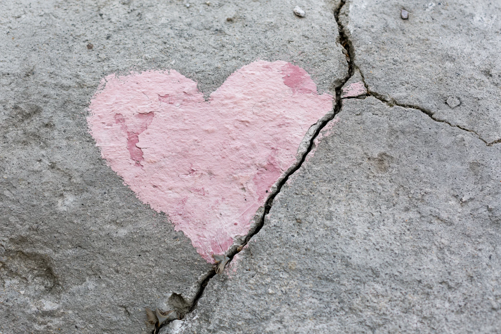 Faded pink heart painted on cracked concrete pavement