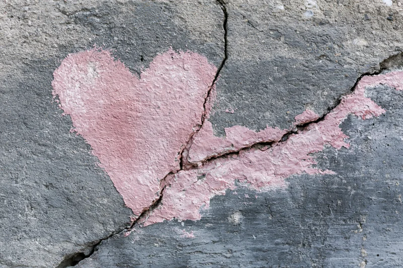 Faded pink heart painted on cracked concrete wall
