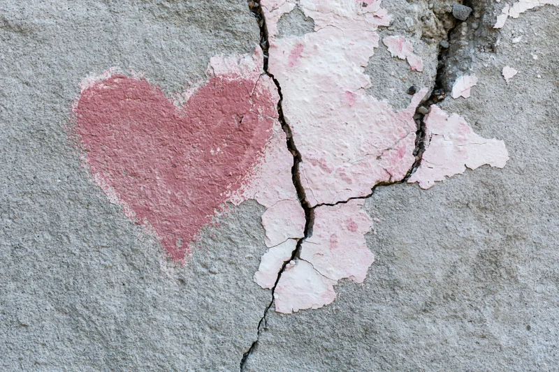 Faded pink heart painted on cracked concrete wall