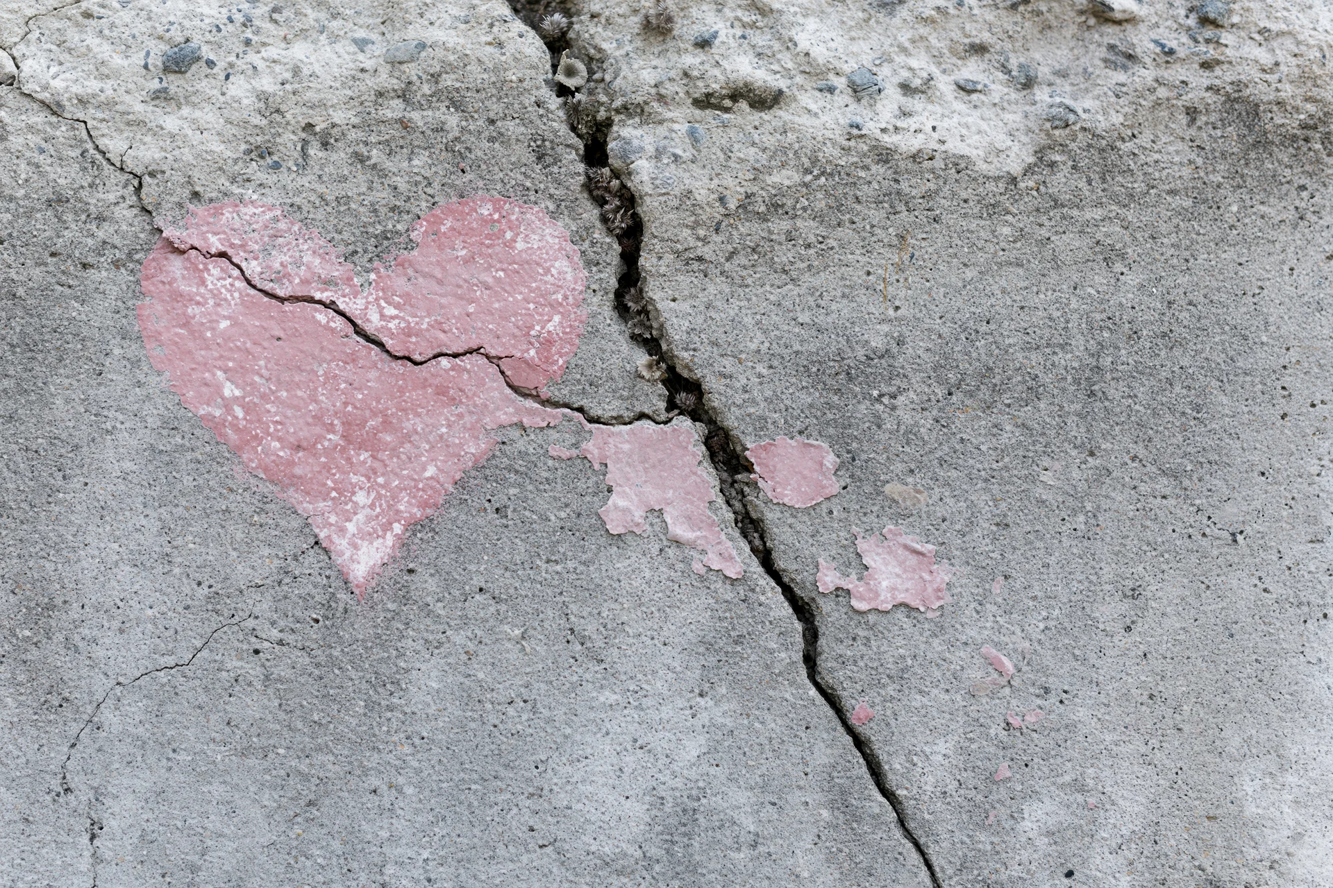 Broken pink heart painted on cracked concrete surface