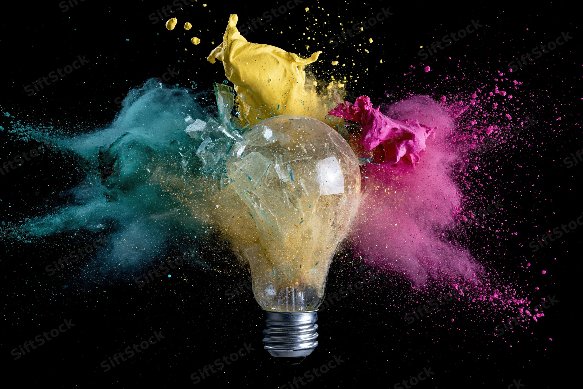 Lightbulb shattering mid-air with colorful powder exploding outward against black background