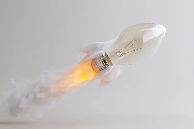 Lightbulb with rocket fins launching with flame and smoke against white background