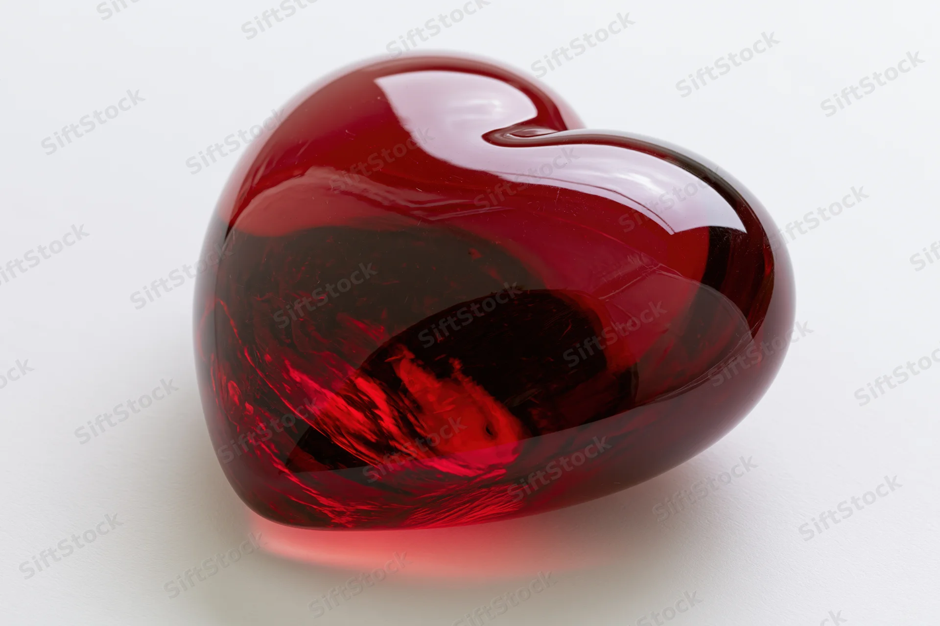 Glossy red glass heart sculpture on white background