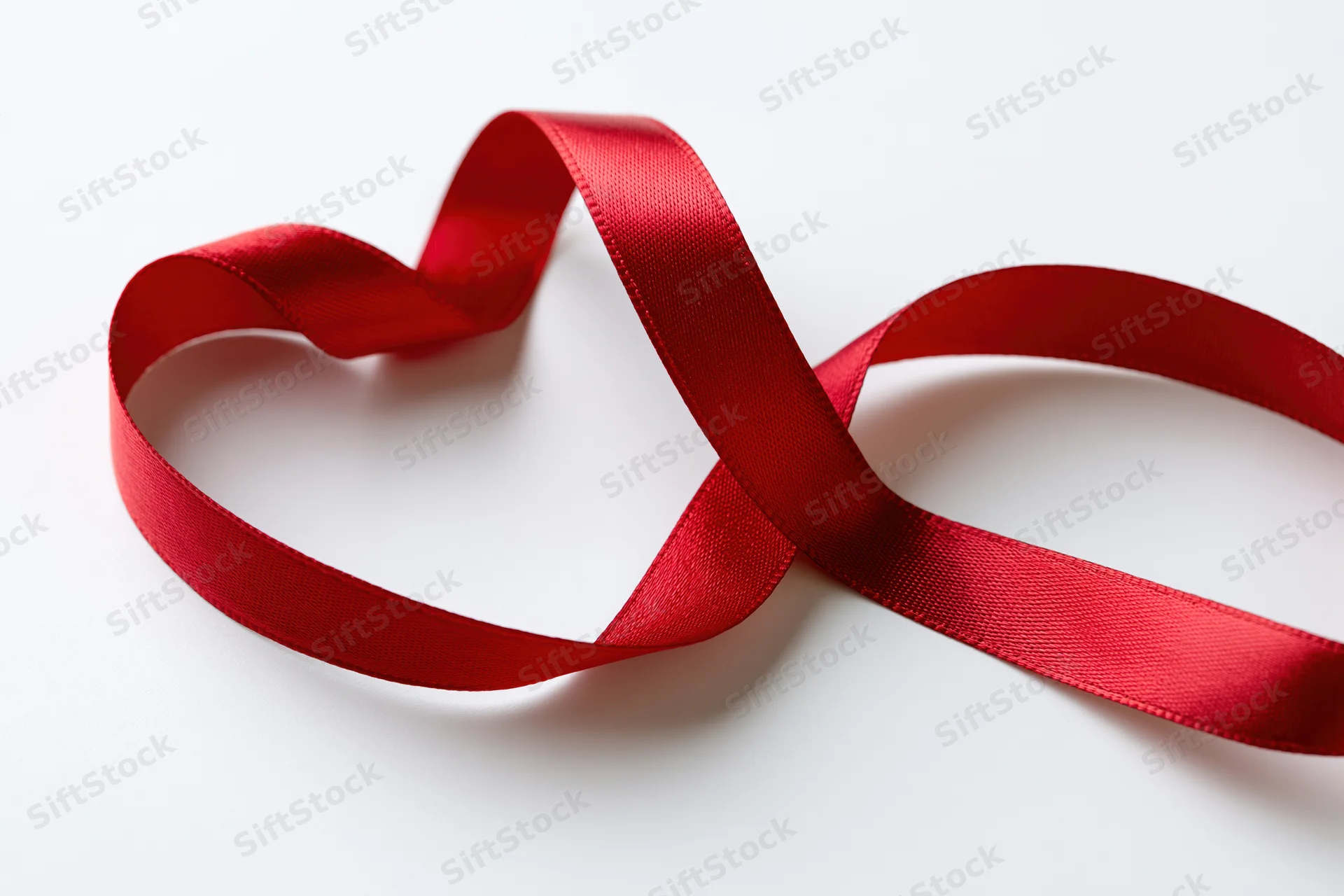 Red satin ribbon curled into a heart shape on white background