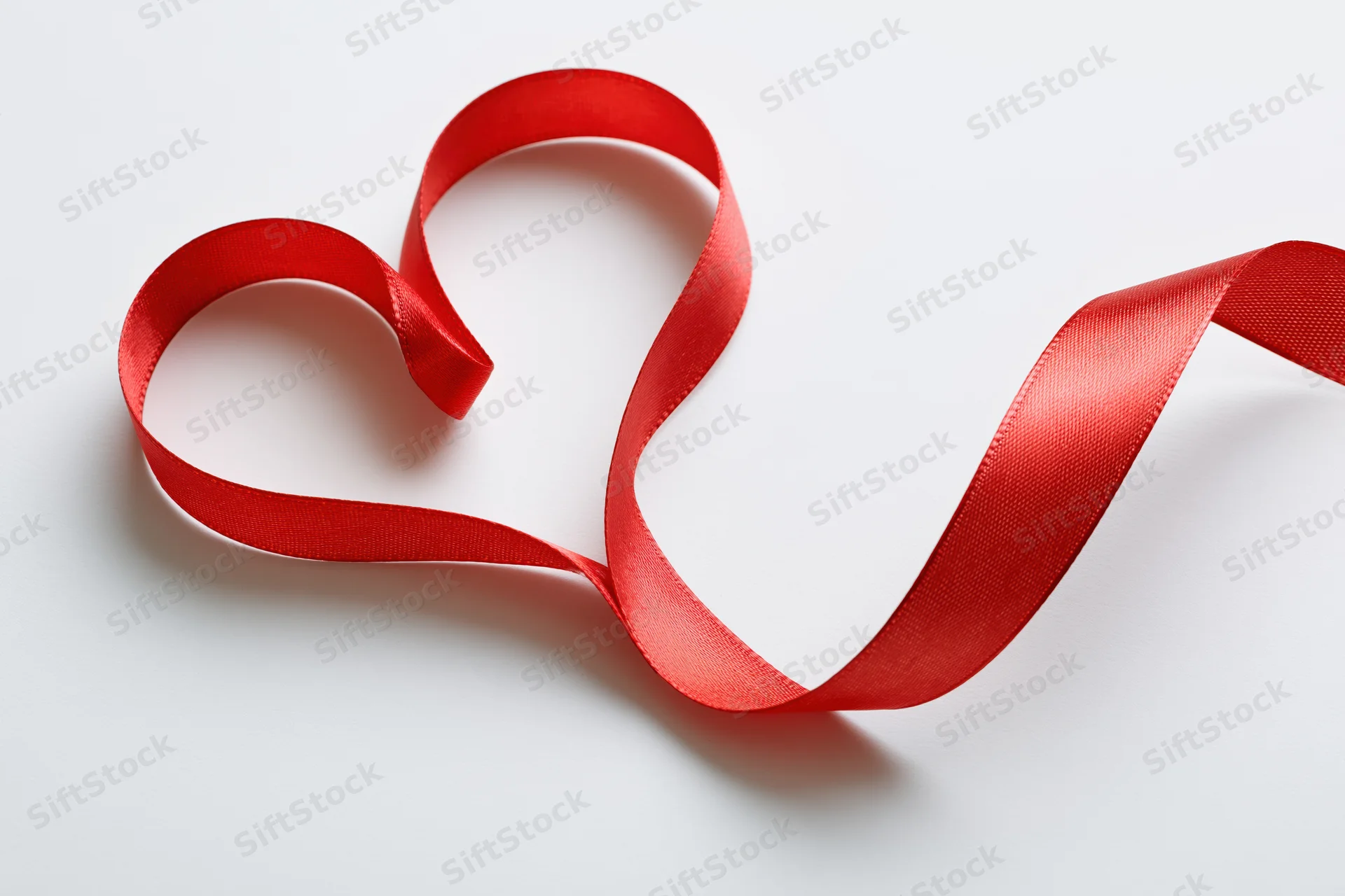 Red satin ribbon shaped into a heart on white surface