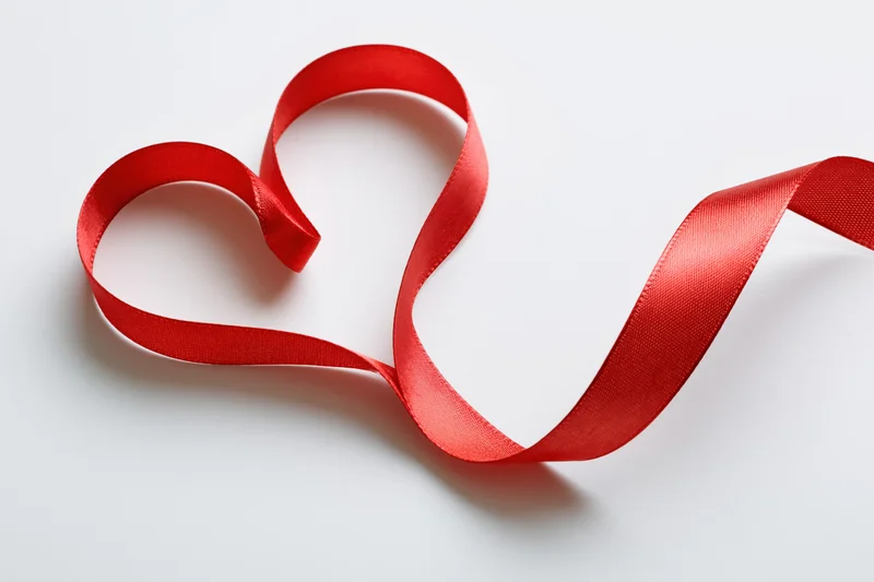 Red satin ribbon shaped into a heart on white surface