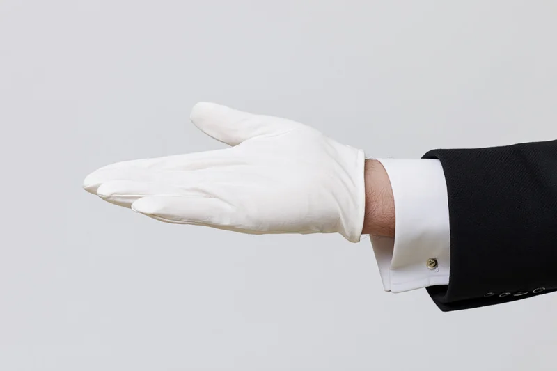 Hand in white glove extended palm-up in offering gesture against plain background