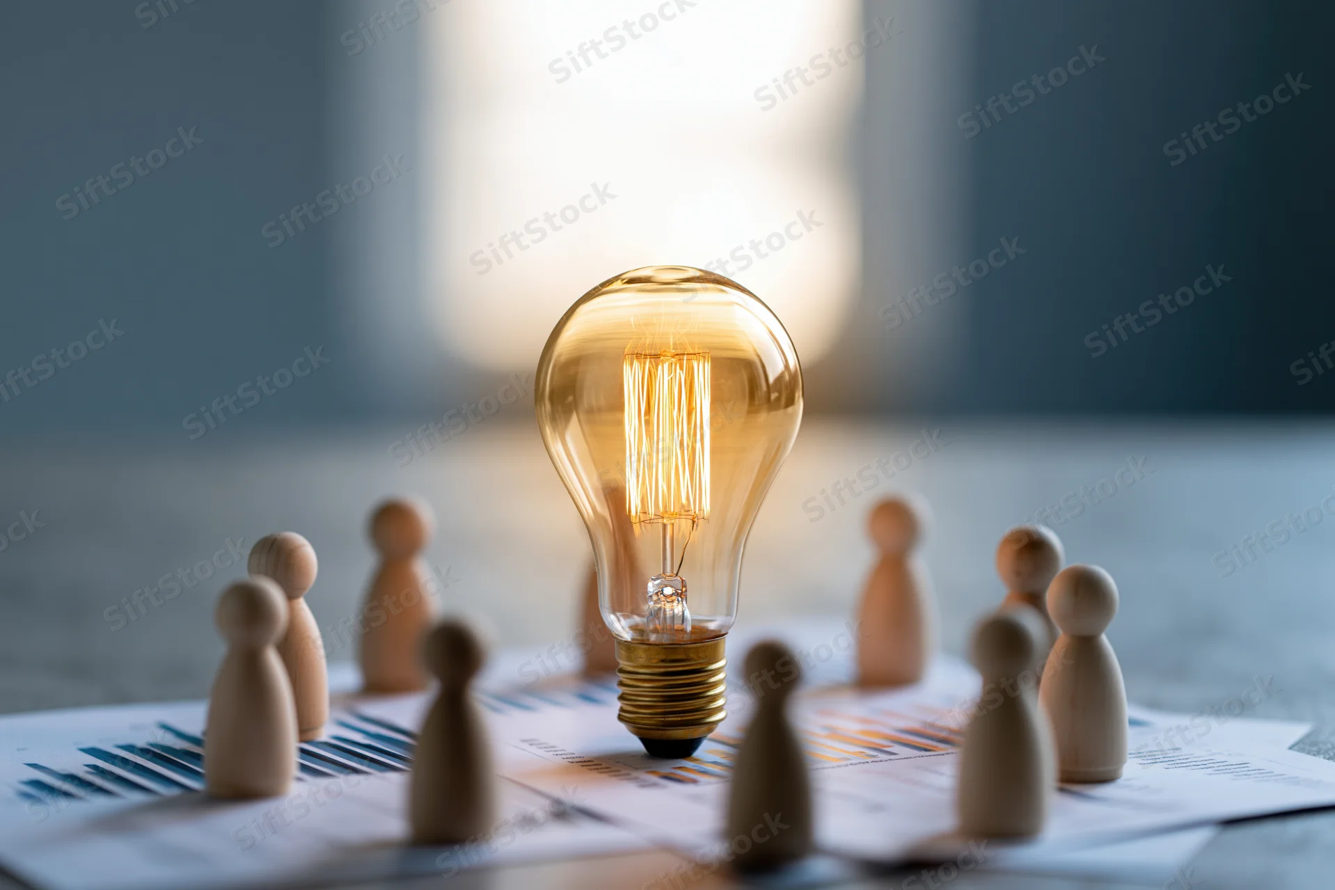 Glowing edison filament bulb on printed bar chart surrounded by wooden figurines on office desk