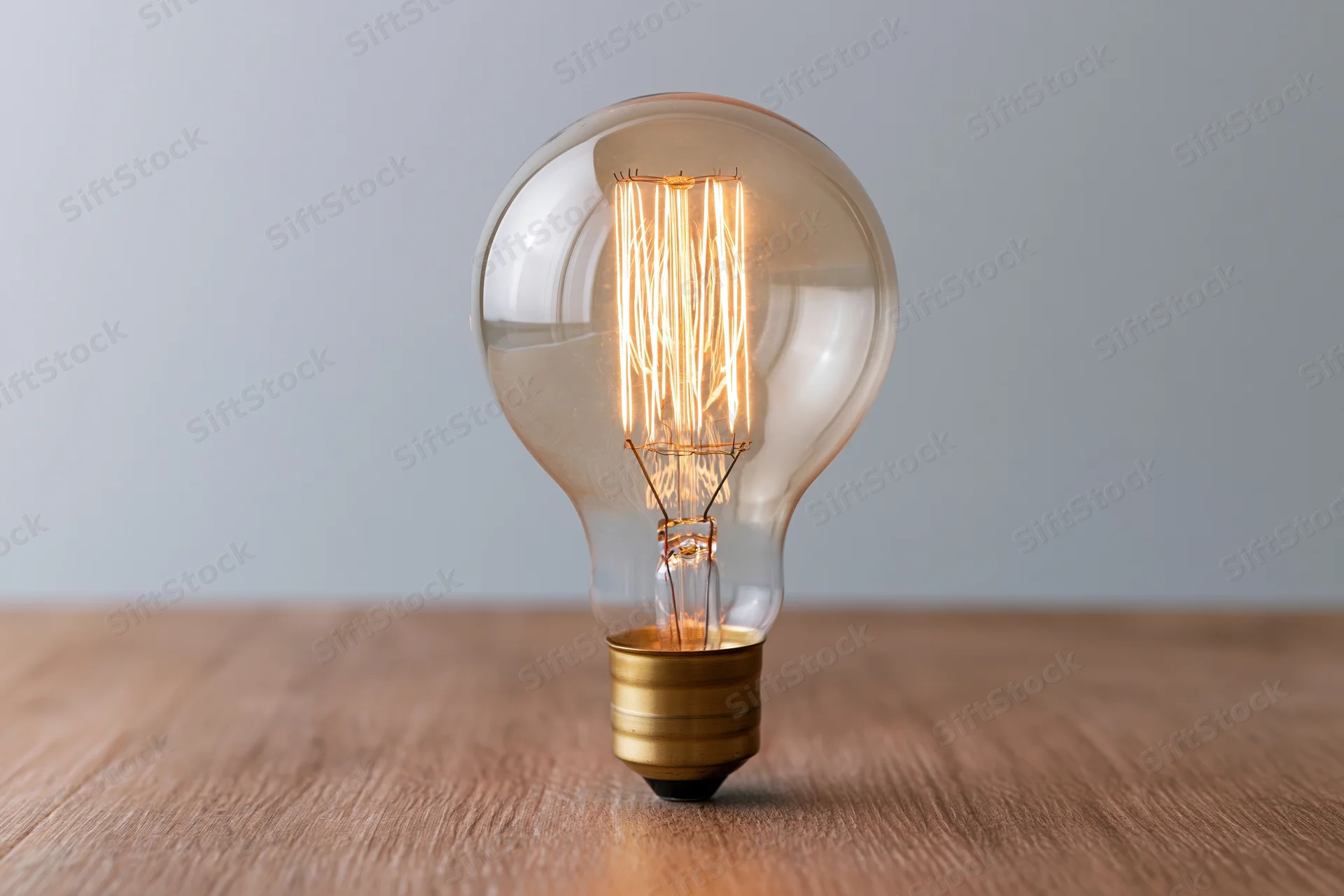 Glowing edison filament lightbulb on wooden table surface