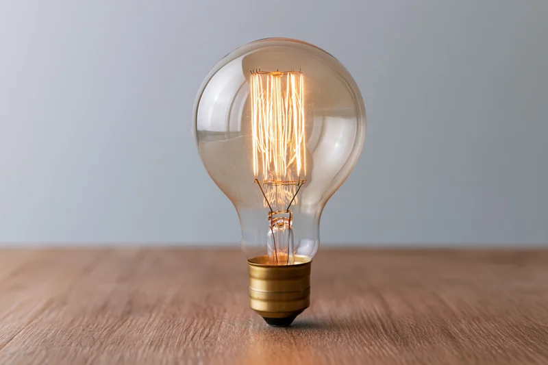 Glowing edison filament lightbulb on wooden table surface