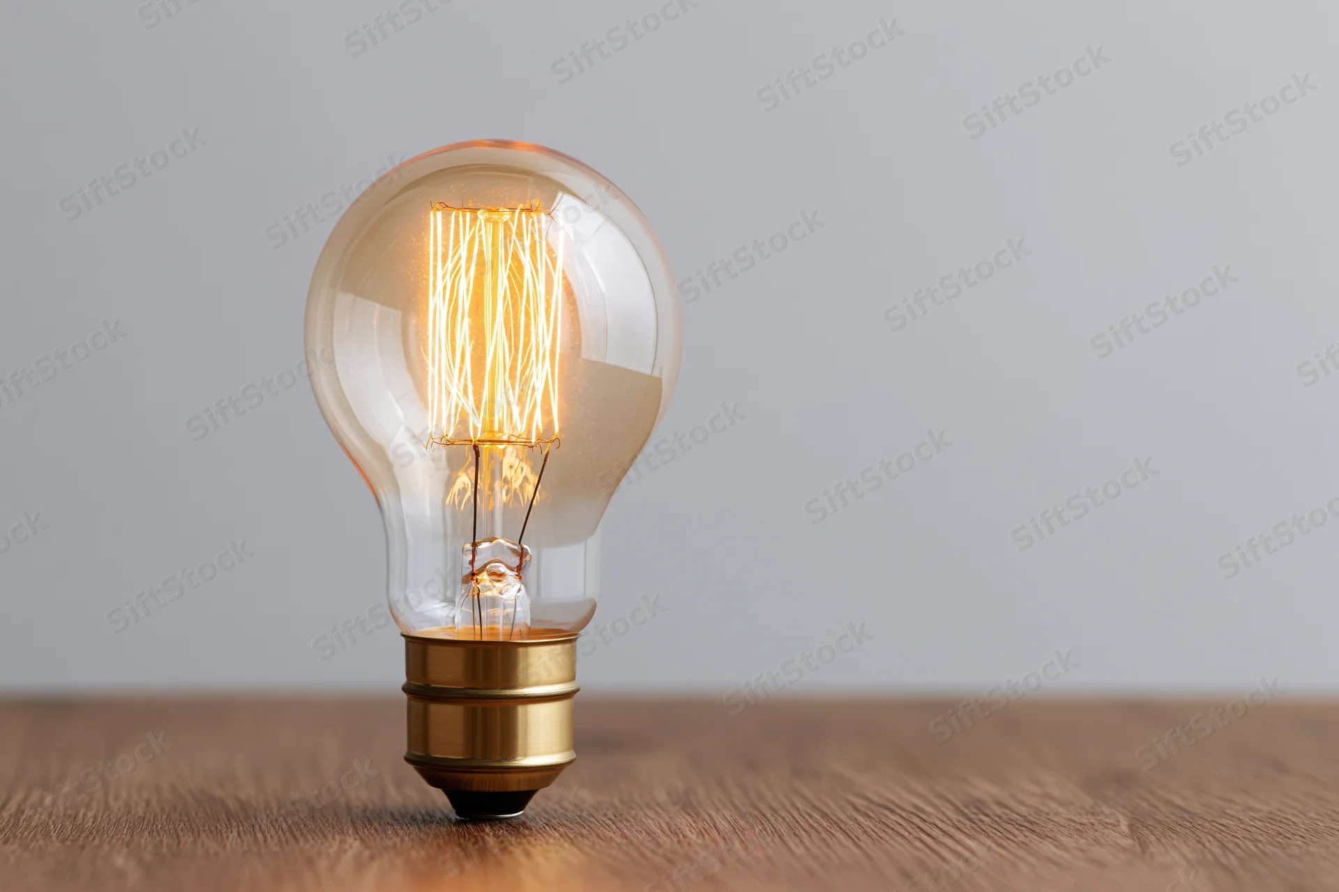 Glowing edison filament lightbulb on wooden surface with copyspace