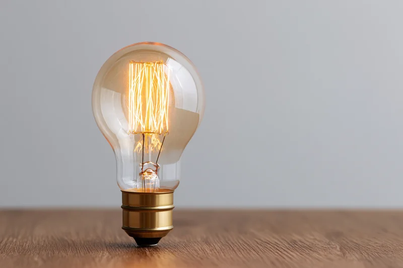 Glowing edison filament lightbulb on wooden surface with copyspace