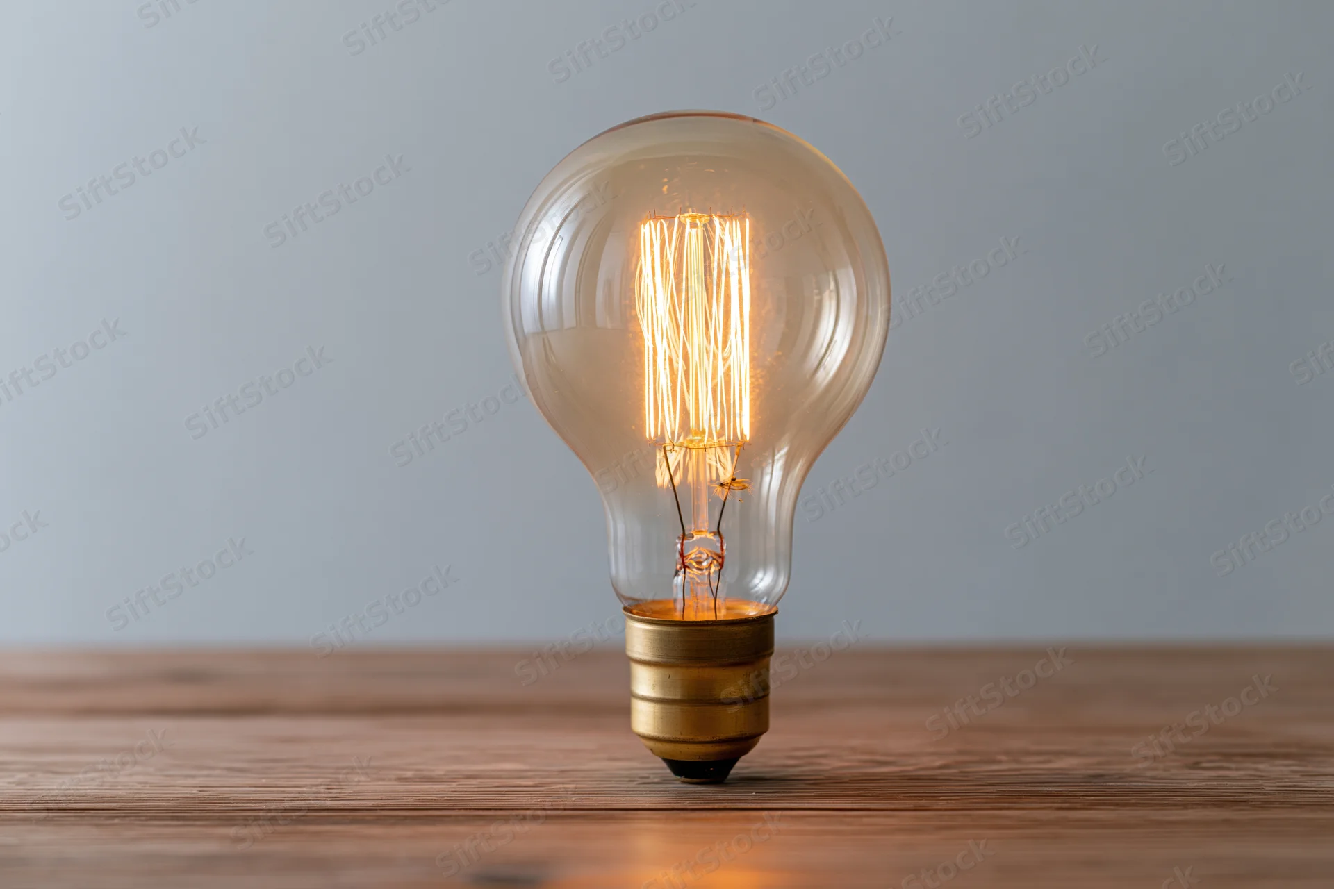 Glowing edison filament lightbulb on wooden table surface