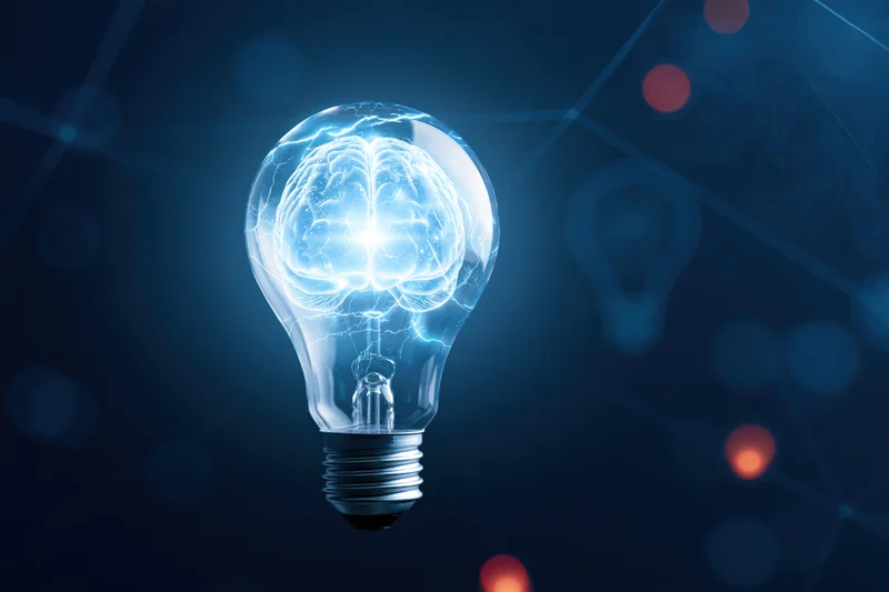 Glowing lightbulb containing a luminous brain illustration against a dark digital background
