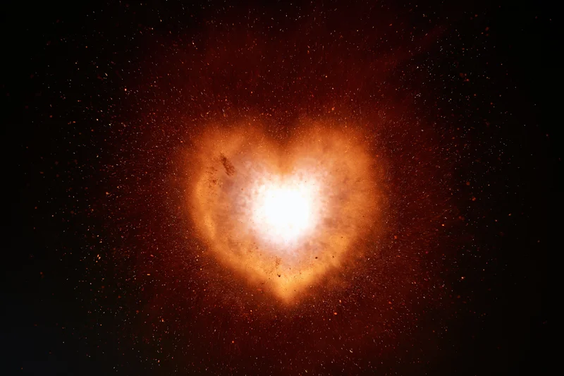 Glowing heart-shaped light burst with red-orange particles against dark background