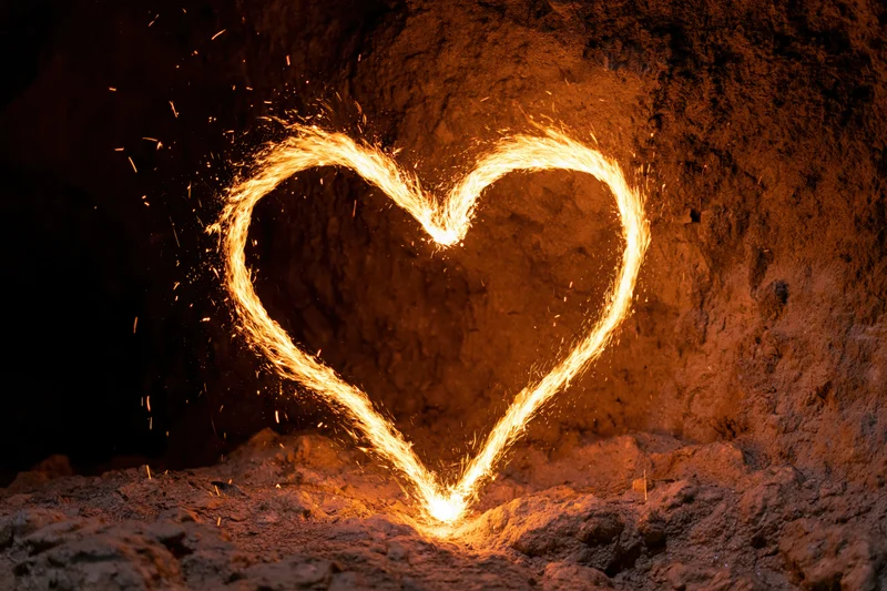 Glowing heart shape traced in fire and embers against a rough rock wall in a cave
