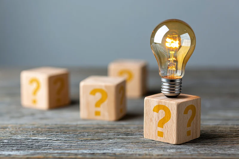 Glowing lightbulb on wooden cube with question marks, arranged on textured surface