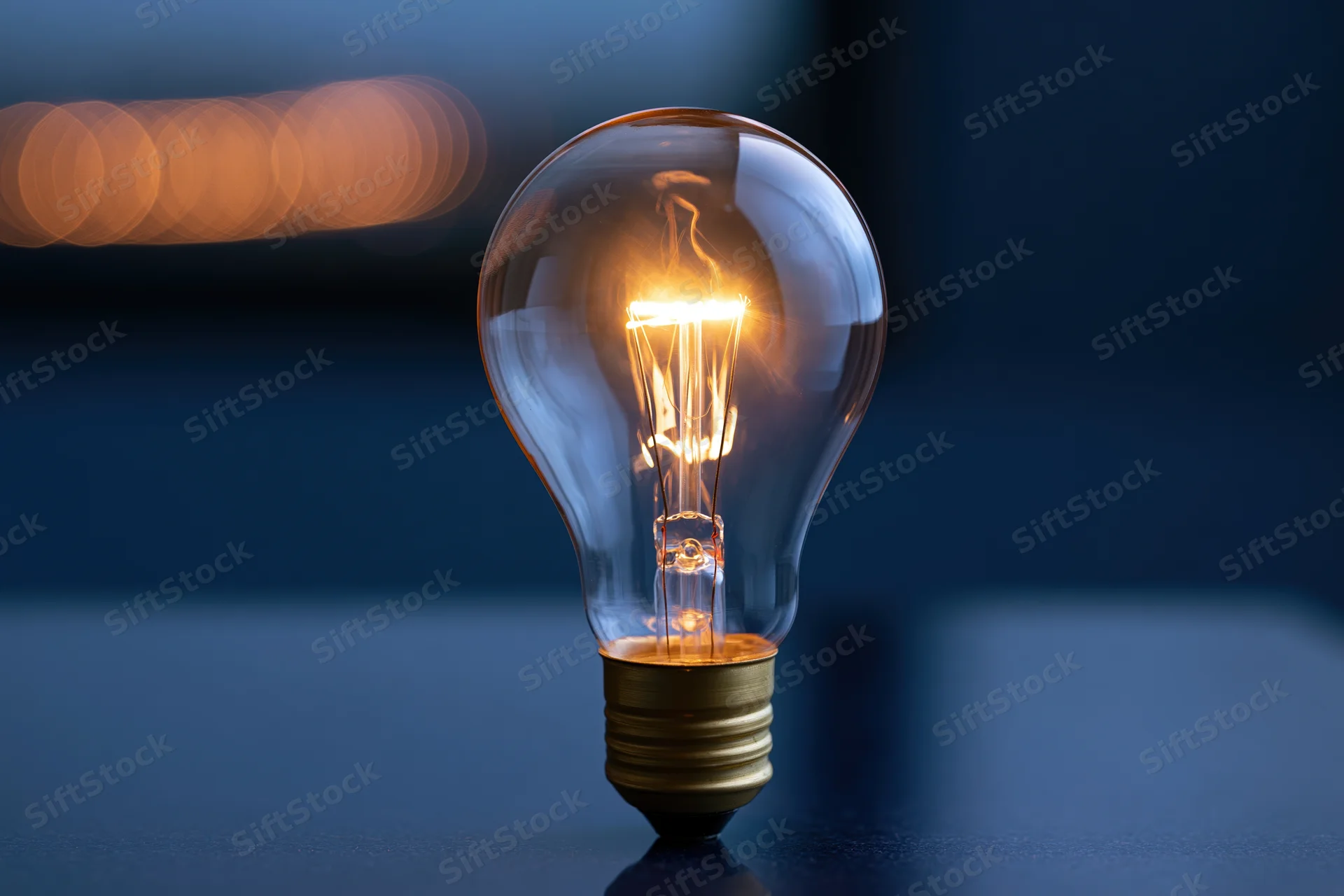Glowing incandescent light bulb on a dark reflective surface with bokeh lights in the background