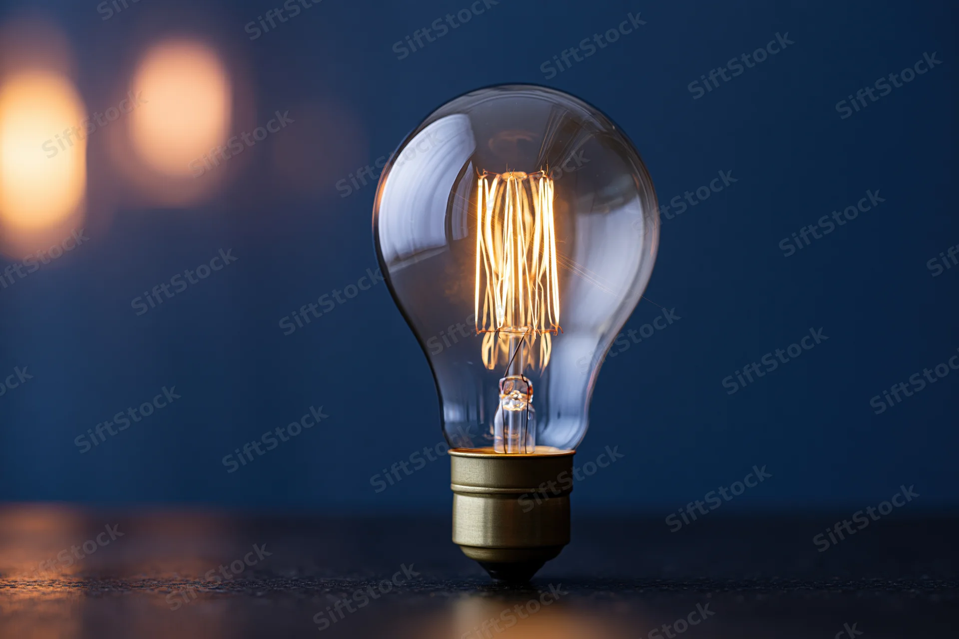 Glowing incandescent light bulb with visible filament on dark reflective surface
